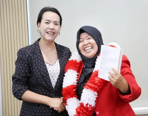 Dr. Sofiawati berkalung bunga merah putih sambil memegang buku, tersenyum lebar berfoto bersama CEO dalam perjalanan penghargaan ke China